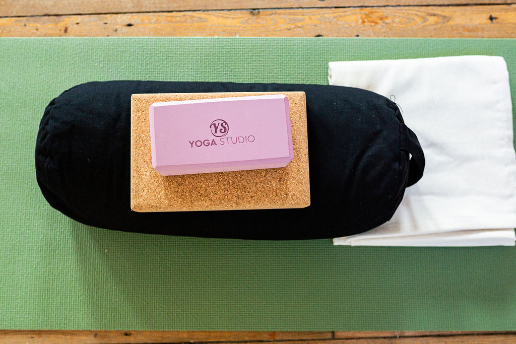 A bolster, cork block, foam block and blanket on a green yoga mat